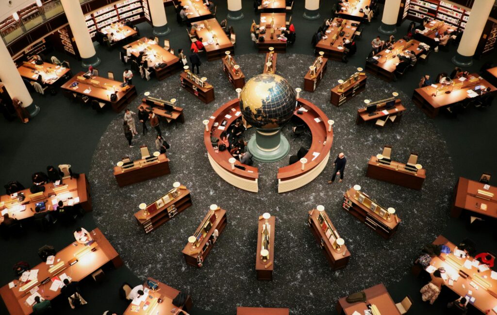 Busy library interior with a large globe centerpiece and people working at wooden tables. High angle view.