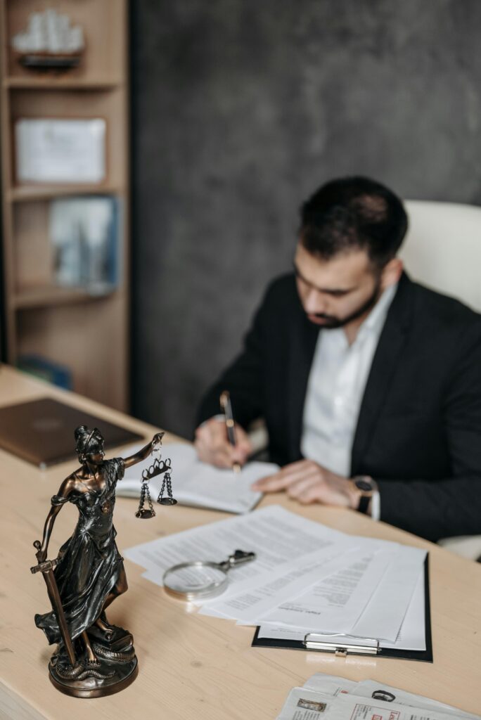 A lawyer concentrates on paperwork in an office; legal statue visible on desk.